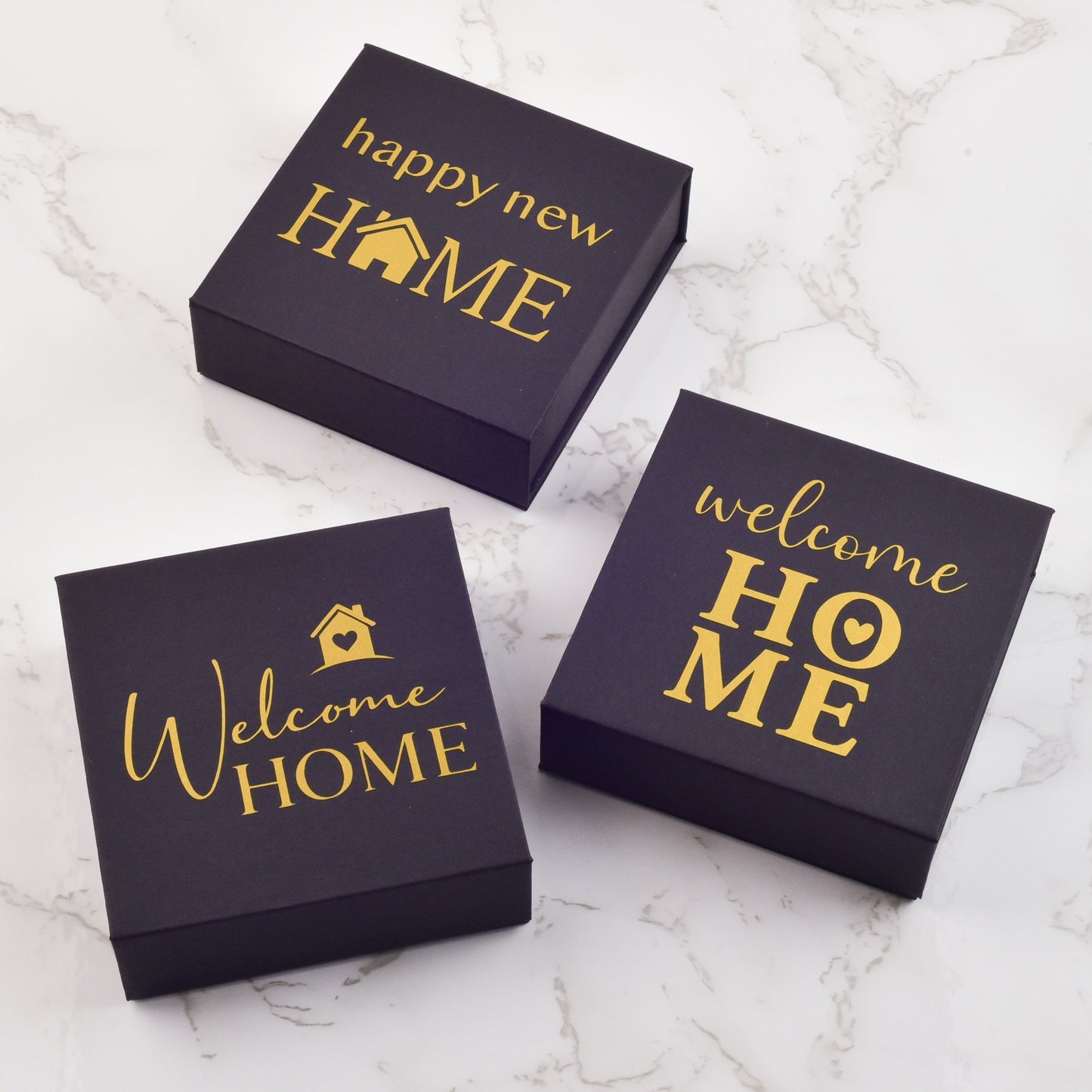 Three boxes with 'Welcome Home' and 'Happy New Home' text on a marble surface to gift keys at closing.