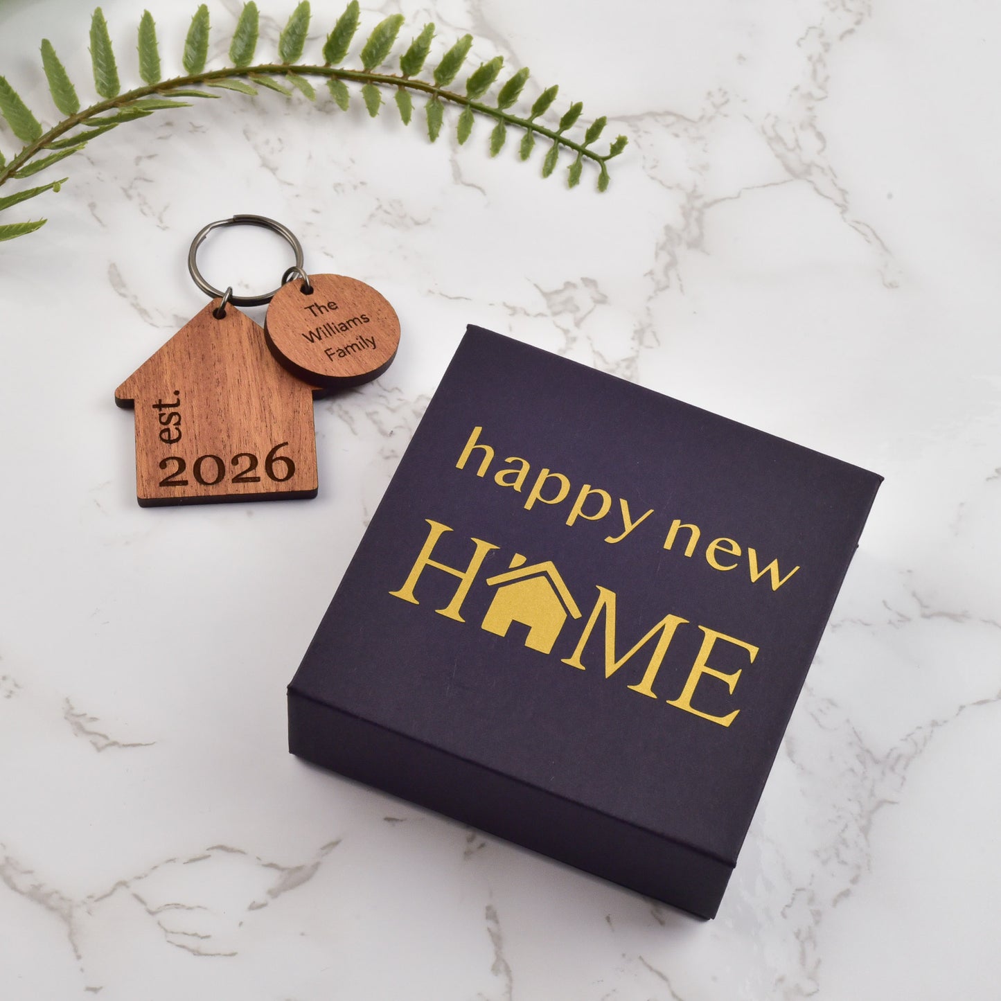 Wooden keychain with house design and 'happy new HOME' box on a marble surface 