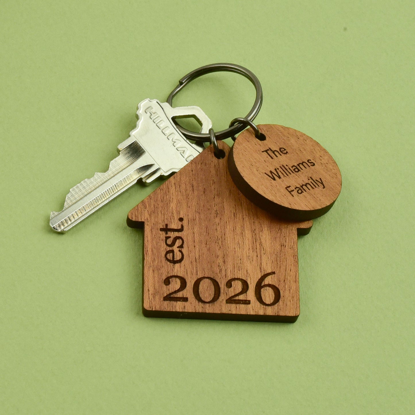 A home shaped wooden keychain engraved with a family name and year, attached to a metal keyring