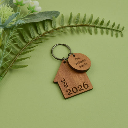 Personalized home-shaped wooden keychain engraved with a family name and a year.