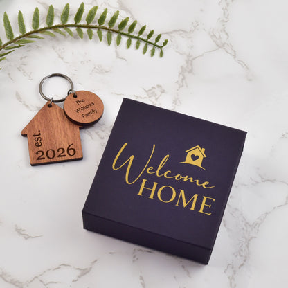 Wooden keychain with engraved text on a 'Welcome Home' card with gold text, placed on a marble surface. 